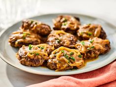 meatballs covered in sauce on a plate with a red napkin and wine glass next to it