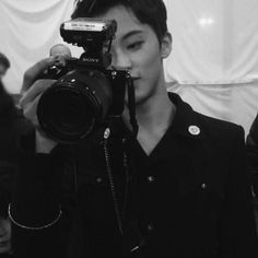 a young man holding a camera up to his face in front of a white curtain