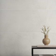 a vase sitting on top of a table next to a book and planter in front of a white tiled wall