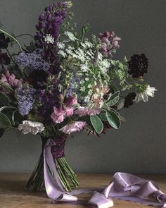 a vase filled with lots of purple flowers on top of a wooden table next to a ribbon