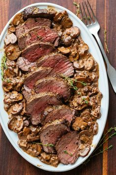 steak and mushrooms on a white platter with a fork next to it, ready to be eaten