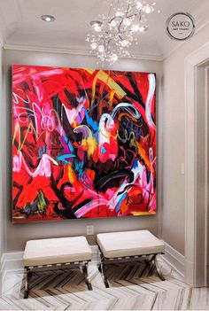 a large painting hanging on the wall in a room with two stools and a chandelier