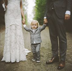 a little boy holding the hand of his mother and father as they walk down a dirt road