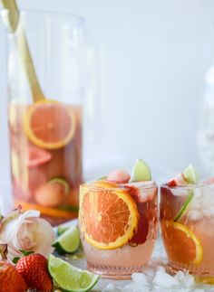 two glasses filled with drinks and garnished with orange slices, limes, and strawberries