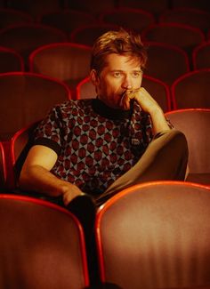 a man is sitting in an empty auditorium with his hand on his chin and looking at the camera