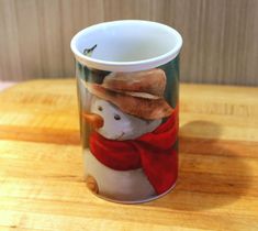 a coffee cup with a snowman on it sitting on top of a wooden table