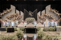 a stage set up for a wedding with floral arrangements and chandeliers on the wall