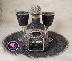 a bottle and three glasses sitting on top of a black tray with silver sequins