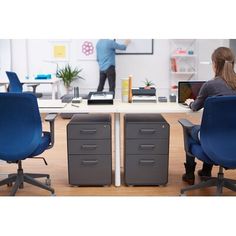 two people sitting at desks in an office with blue chairs and grey filing cabinets