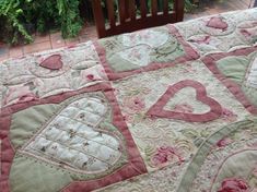 a quilted bed with hearts on it and a wooden bench in the back ground