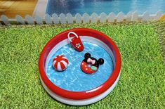 a mickey mouse and minnie mouse in a kiddie pool on the grass next to a white picket fence