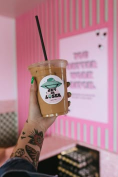 a person holding up a drink in front of a pink wall with writing on it