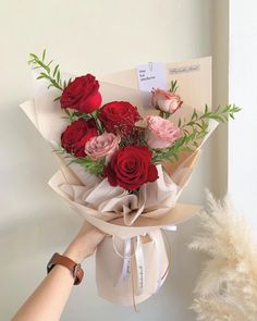 a bouquet of red and pink roses is held up by someone's hand in front of a white wall