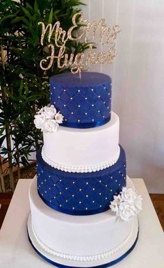 a three tiered blue and white wedding cake with flowers on the side, sitting on top of a table