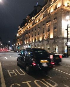 cars are driving down the street in front of a building at night with lights on