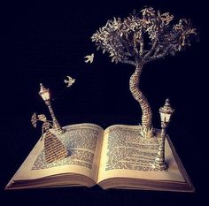 an open book that has some kind of tree on top of it with birds flying around