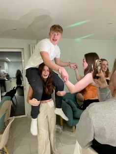 a group of people standing around each other in a living room with one person on the back of someone's shoulders