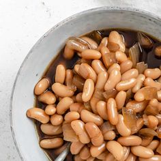 a bowl filled with lots of beans on top of a white countertop next to a silver spoon