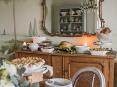 a dining room table with plates and bowls on it, candles in front of the buffet