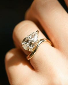 a person's hand holding a ring with a pear shaped diamond