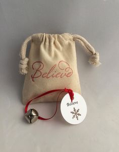 a small bag with a bell on it and a tag attached to the back that says believe