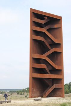 a tall brown sculpture sitting in the middle of a field next to a person on a skateboard