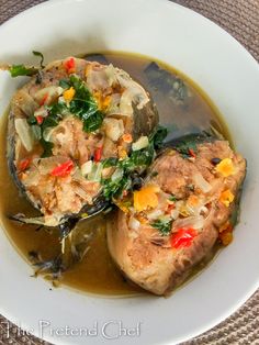 two pieces of meat with vegetables and sauce in a white bowl