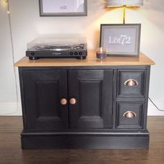 a record player sitting on top of a black cabinet next to a lamp and pictures