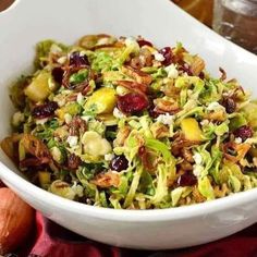 a white bowl filled with shaved brussels sprouts, cranberries and nuts