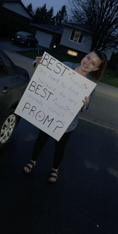 a woman holding up a sign that says best from? in front of her car