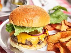 a cheeseburger with lettuce, tomato and onion on a plate next to potato chips