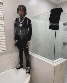 a man standing on the edge of a bathtub next to a shower stall and wearing black sneakers