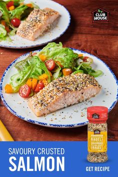 two white plates topped with salmon and salad next to a jar of seasoning on a wooden table