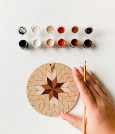 a hand holding a paintbrush next to a wooden plate with different colors on it