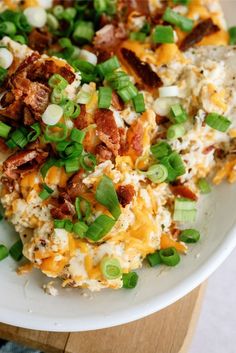 a white plate topped with rice covered in bacon and scalloped green onions on top of a wooden cutting board