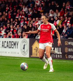 a female soccer player is running with the ball in front of an arena full of people