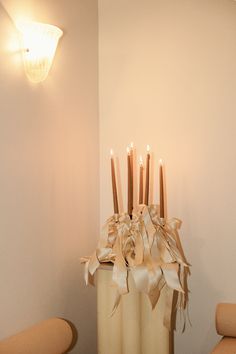 a tall vase with candles in it sitting on a table next to two chairs and a wall light