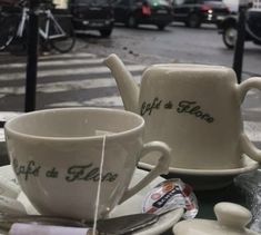 two coffee cups and saucers sitting on a table in front of a city street