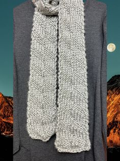 a knitted scarf hanging on a clothes hanger with mountains in the back ground