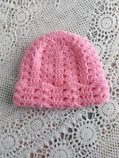 a pink crocheted hat sitting on top of a white doily covered table