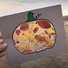 a hand holding up a paper cutout with leaves and acorns on it