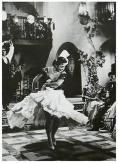 an old black and white photo of a woman in a dress dancing on the floor