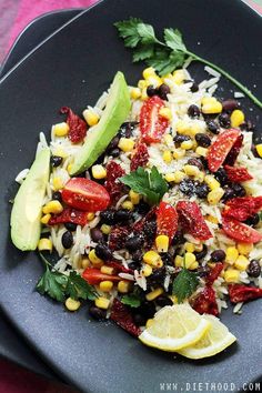 a black plate topped with rice, beans and avocado next to lime wedges