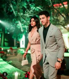 a man and woman in formal wear walking down a path at night with green lights behind them