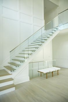 a white staircase with glass railing and bench in the middle, next to it is an empty room