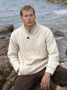 This mans shawl collar cable knit sweater is knit using traditional knitting patterns from Ireland. The “V” neck shawl collar is the main feature of this Irish sweater. It is completed with the use of an old-style button closure. The diamond knitting pattern along the body is said to represent wealth and success. The traditional cable pattern symbolizing fisherman’s ropes unite the past with the modern-day. The use of the herringbone stitch along the body and the length of the arms is further li Diamond Knitting Pattern, Irish Wool Sweaters, Irish Knitwear, Sweater With Collar, Irish Hat, Irish Sweater, Irish Style, Pompom Scarf, Shawl Collar Sweater