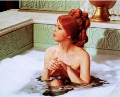 a woman sitting in a bathtub with her hands clasped to her chest and looking off into the distance