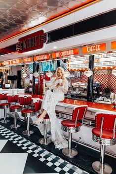 a woman sitting at a diner counter in front of red chairs and neon signs on the ceiling