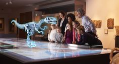 a group of people standing in front of a glass table with a dinosaur skeleton on it