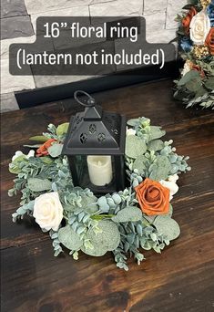 an arrangement of flowers and greenery on a table with a candle in the center